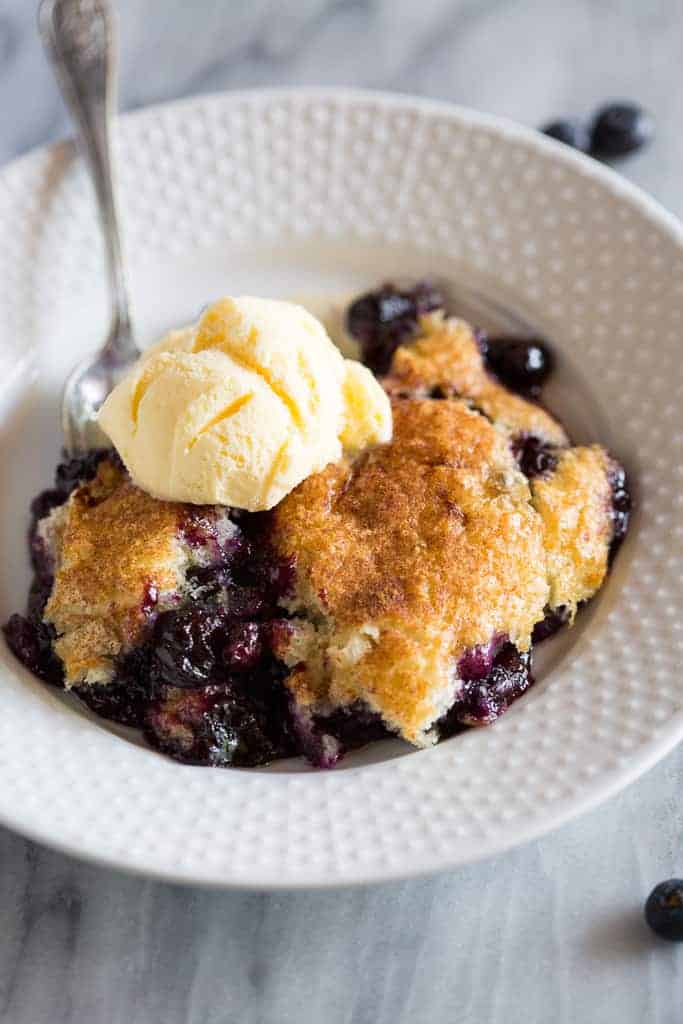 Warm blueberry cobbler served in a bowl with a scoop of vanilla ice cream