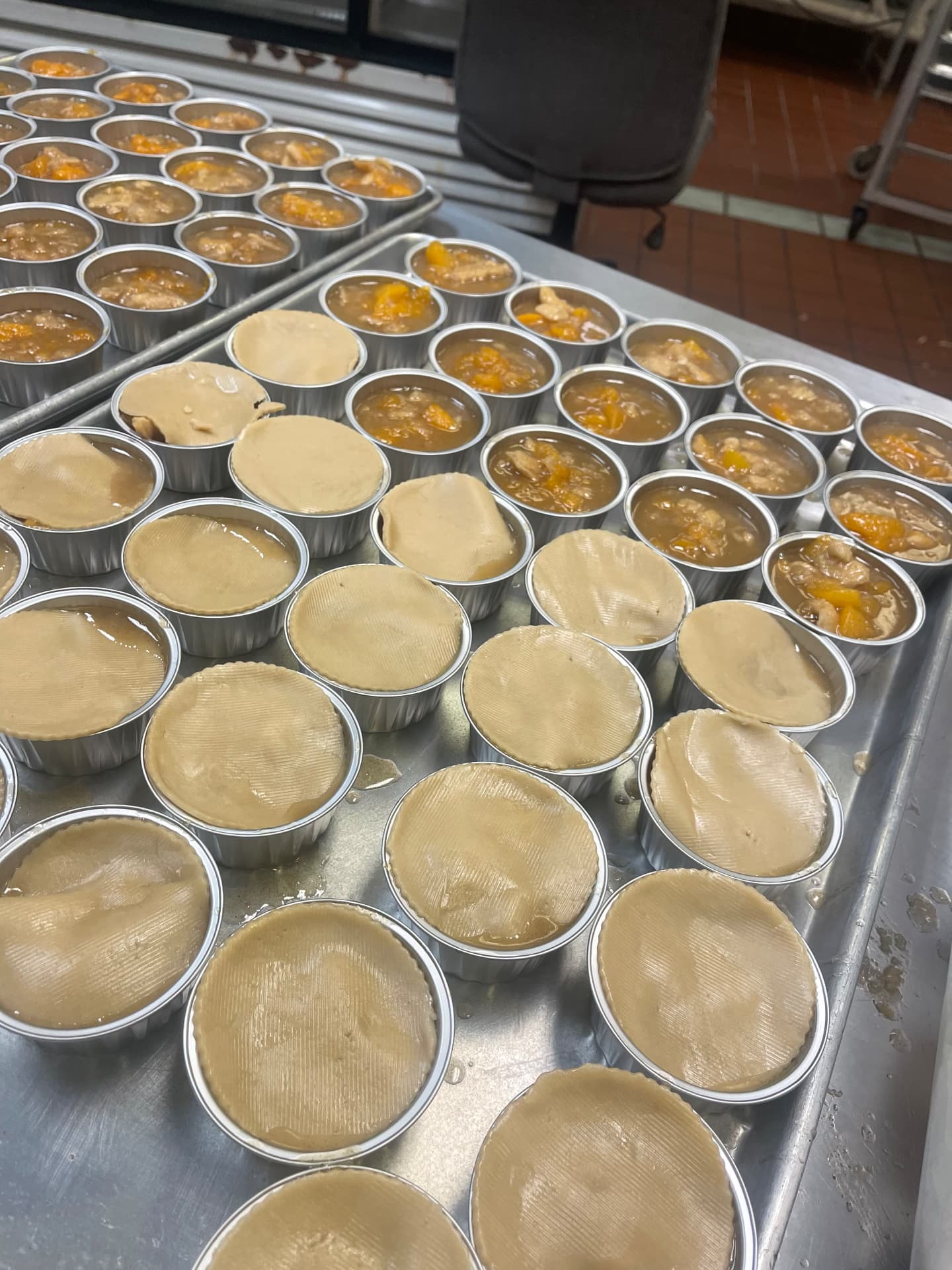 Rows of cobbler tins being filled with fruit and topped with crust